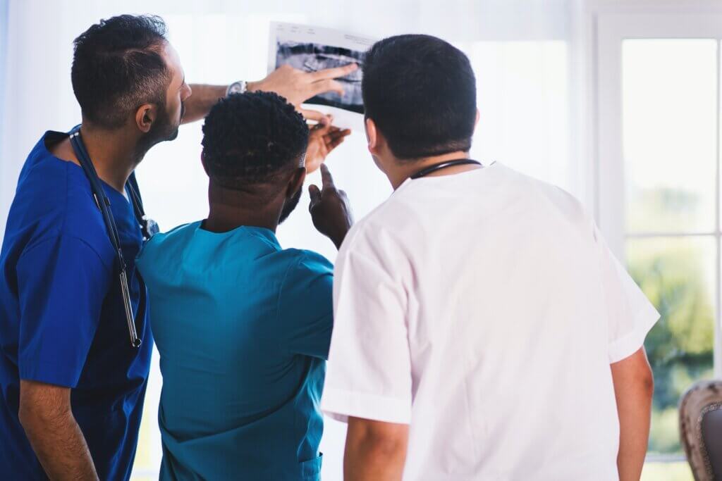 Tre medici, uno di carnagione scura e gli altri due di carnagione bianca, indossando camici e stetoscopi, esaminano un'immagine di scansione radiografica.